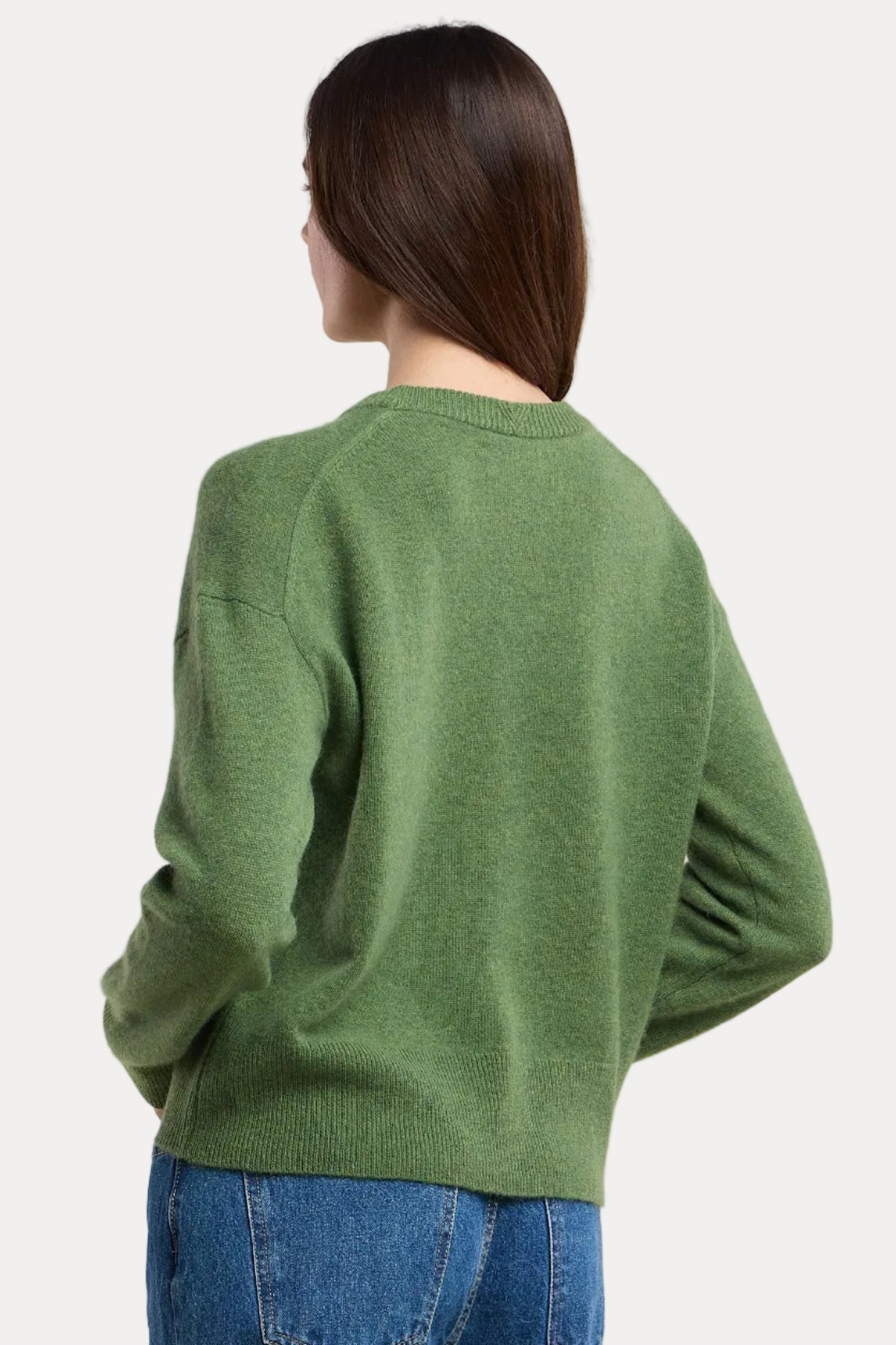 Person wearing a green sweater and blue jeans on a beige background