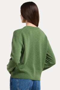 Person wearing a green sweater and blue jeans on a beige background