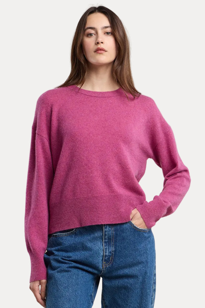Woman wearing a pink sweater and blue jeans on a beige background