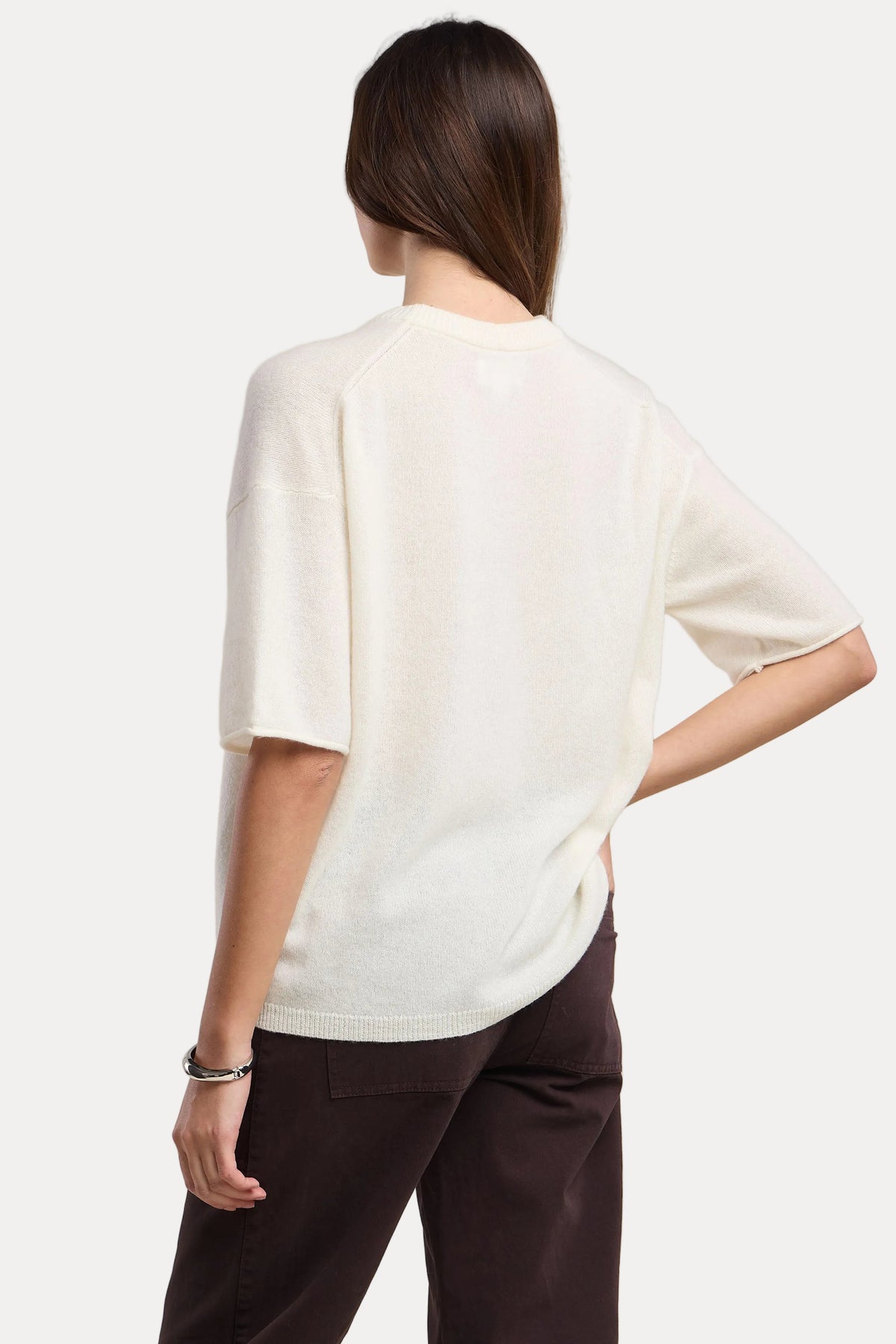 Person wearing a white top and brown pants on a beige background
