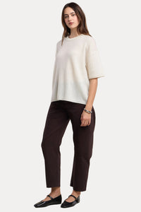 Woman wearing a white top and dark pants on a beige background