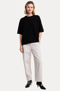 Woman wearing a black top and white pants on a beige background