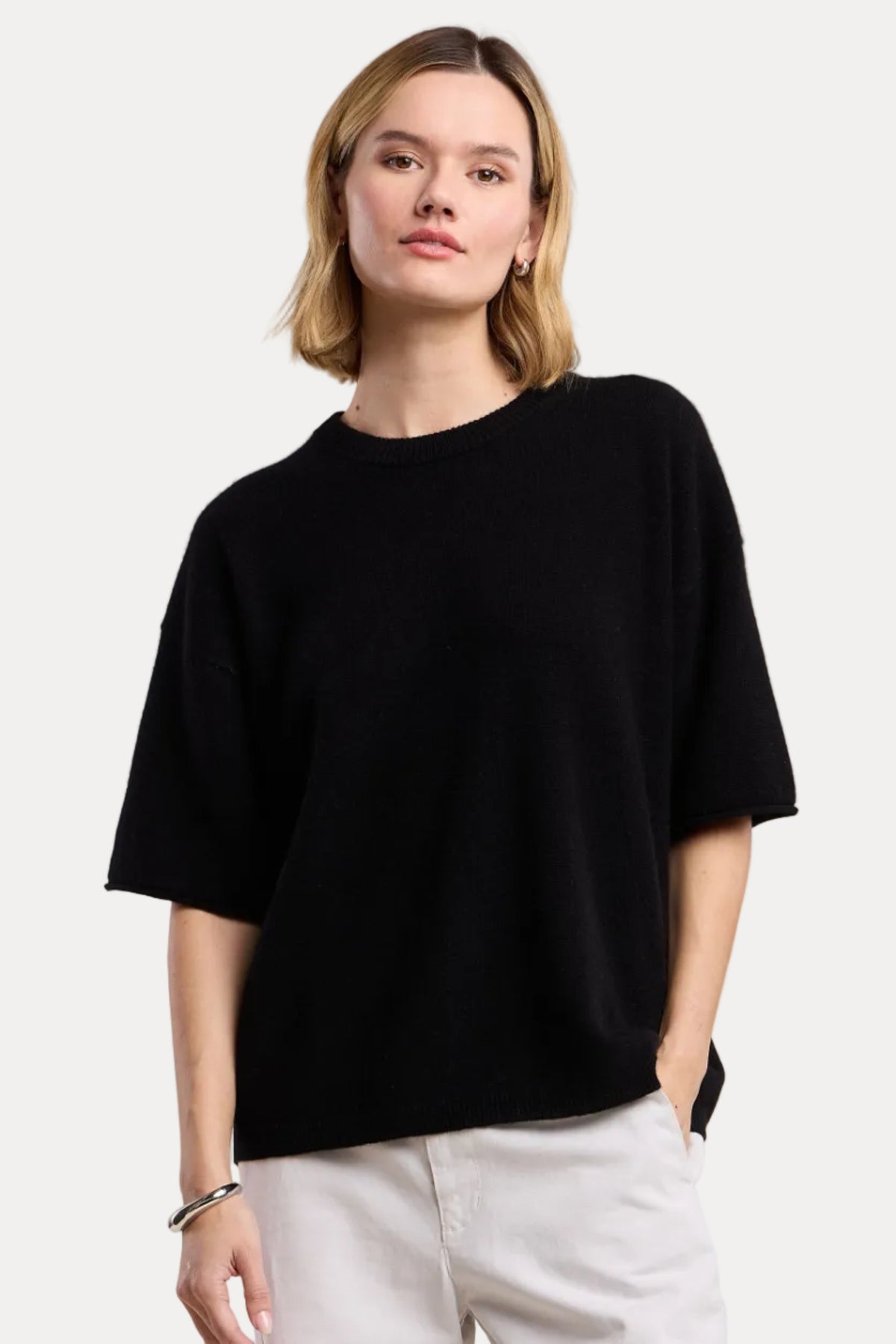 Woman wearing a black oversized sweater and light-colored pants on a beige background