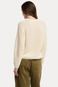 Person wearing a cream sweater and green pants on a plain background