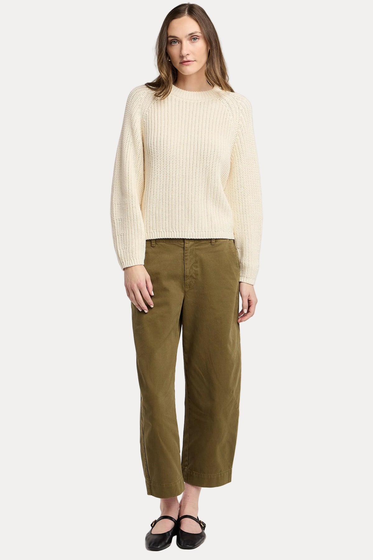 A woman modeling a cream ribbed knit sweater and olive green cropped trousers against a light gray studio background.