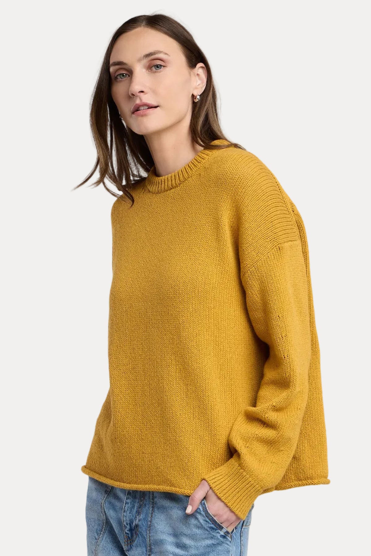 Woman wearing a mustard yellow sweater and blue jeans on a light gray background