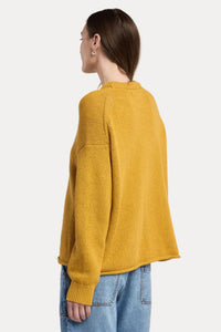 Person wearing a mustard yellow sweater and blue jeans on a plain background