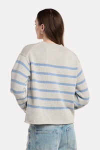 A woman shown from the back wearing a light gray knit sweater with horizontal light blue stripes and light-wash blue jeans, photographed against a plain light gray studio background.
