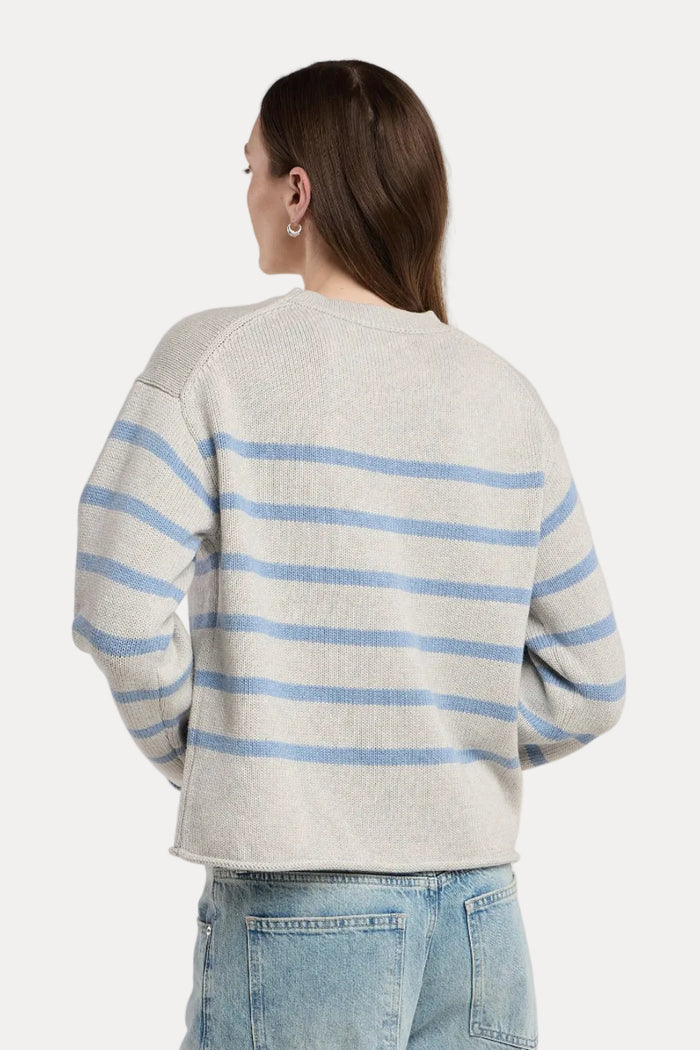 A woman shown from the back wearing a light gray knit sweater with horizontal light blue stripes and light-wash blue jeans, photographed against a plain light gray studio background.