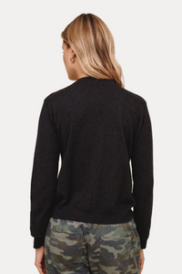 A woman shown from the back wearing a dark charcoal heather knit sweater and camouflage pants, standing against a solid beige studio background.