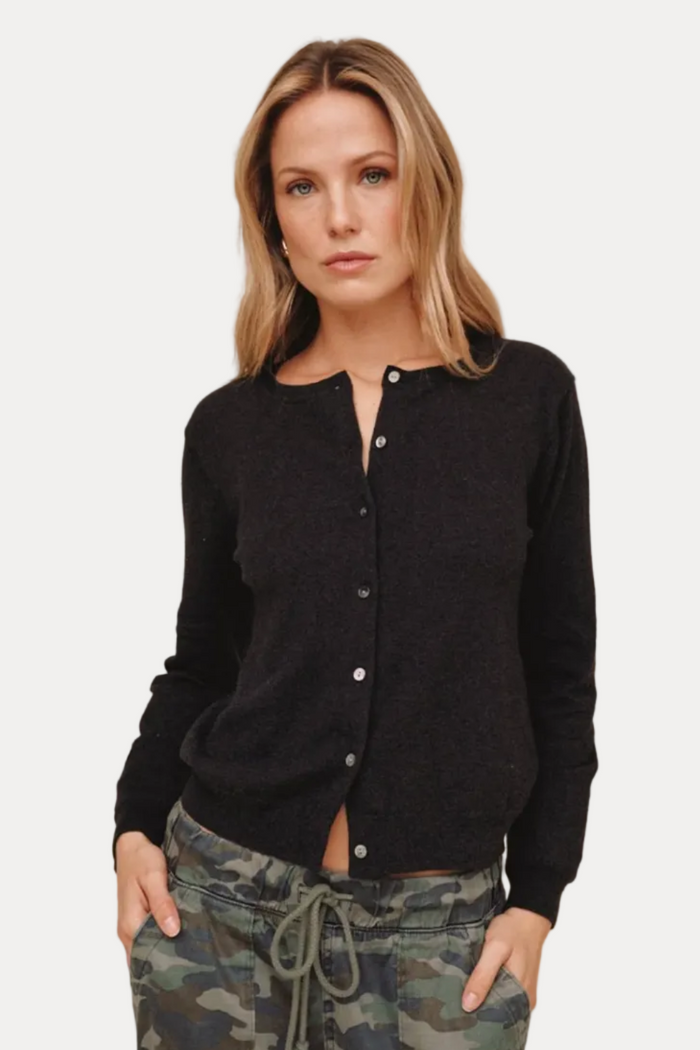 A woman modeling a black long-sleeve button-front cardigan with a relaxed fit, paired with camouflage drawstring pants, against a plain beige studio background.