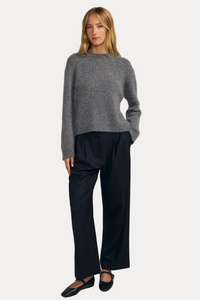 A woman modeling a gray knit sweater and black wide-leg trousers against a solid beige studio background.