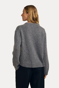A woman shown from the back wearing a heather gray knit sweater and black pants, standing against a plain beige studio background.