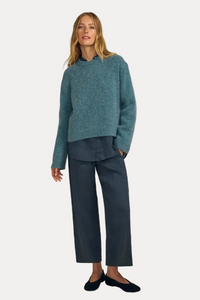 A woman modeling a teal blue knit sweater and dark blue wide-leg trousers against a solid beige studio background.