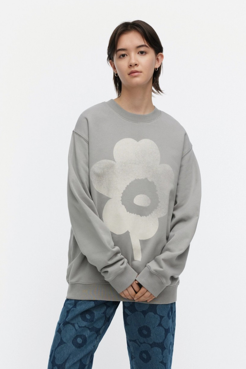 Person wearing a gray sweatshirt with a flower design and blue patterned pants on a white background