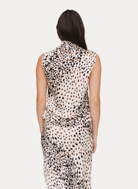 A woman viewed from the back wearing a sleeveless high-neck dress with a black, brown, and beige spotted animal print on a cream background, set against a plain beige studio backdrop.