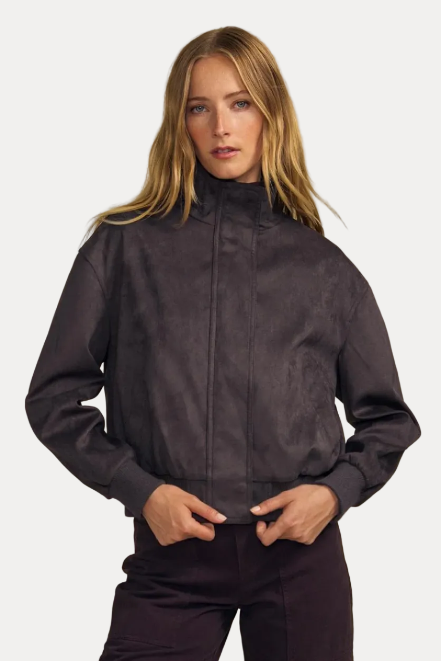 A woman modeling a dark plum zip-up jacket with dark green ribbed cuffs and matching dark plum pants, set against a solid beige studio background.