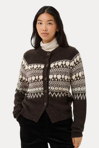 A woman modeling a dark brown and cream patterned knit cardigan sweater over a white turtleneck and black pants, shot against a plain light gray studio background.