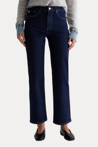 A person wearing dark blue straight-leg denim jeans with a gray knit sweater and black flats, shown from the waist down against a plain light gray studio background.