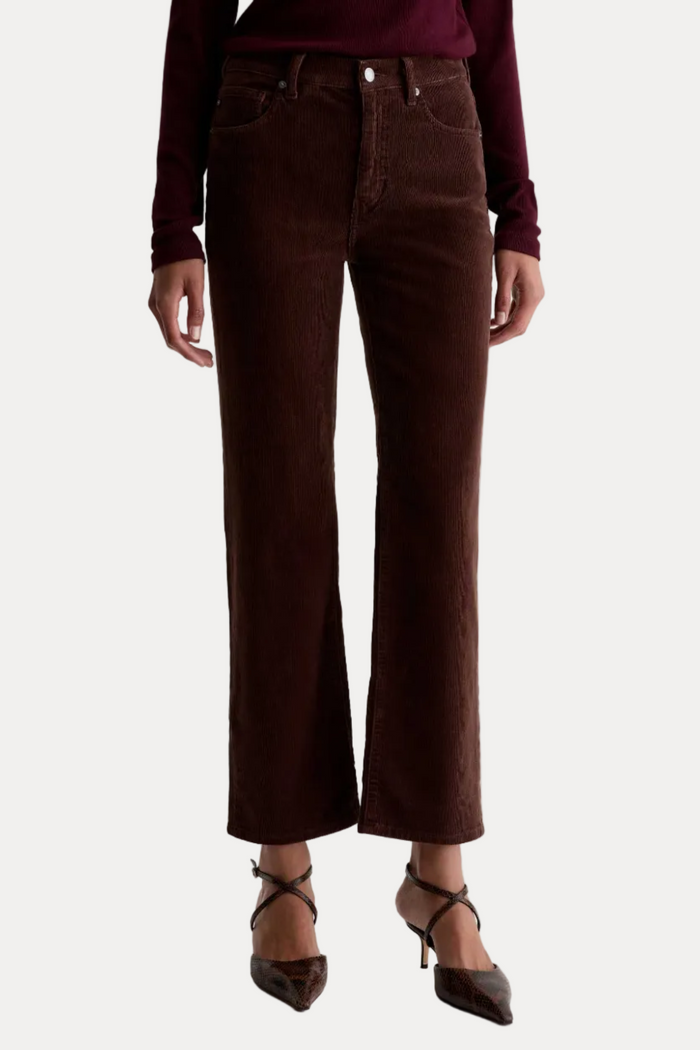 A model is shown from the waist down wearing dark brown corduroy cropped flare jeans, a burgundy long-sleeve top, and brown pointed-toe heels against a plain white studio background.