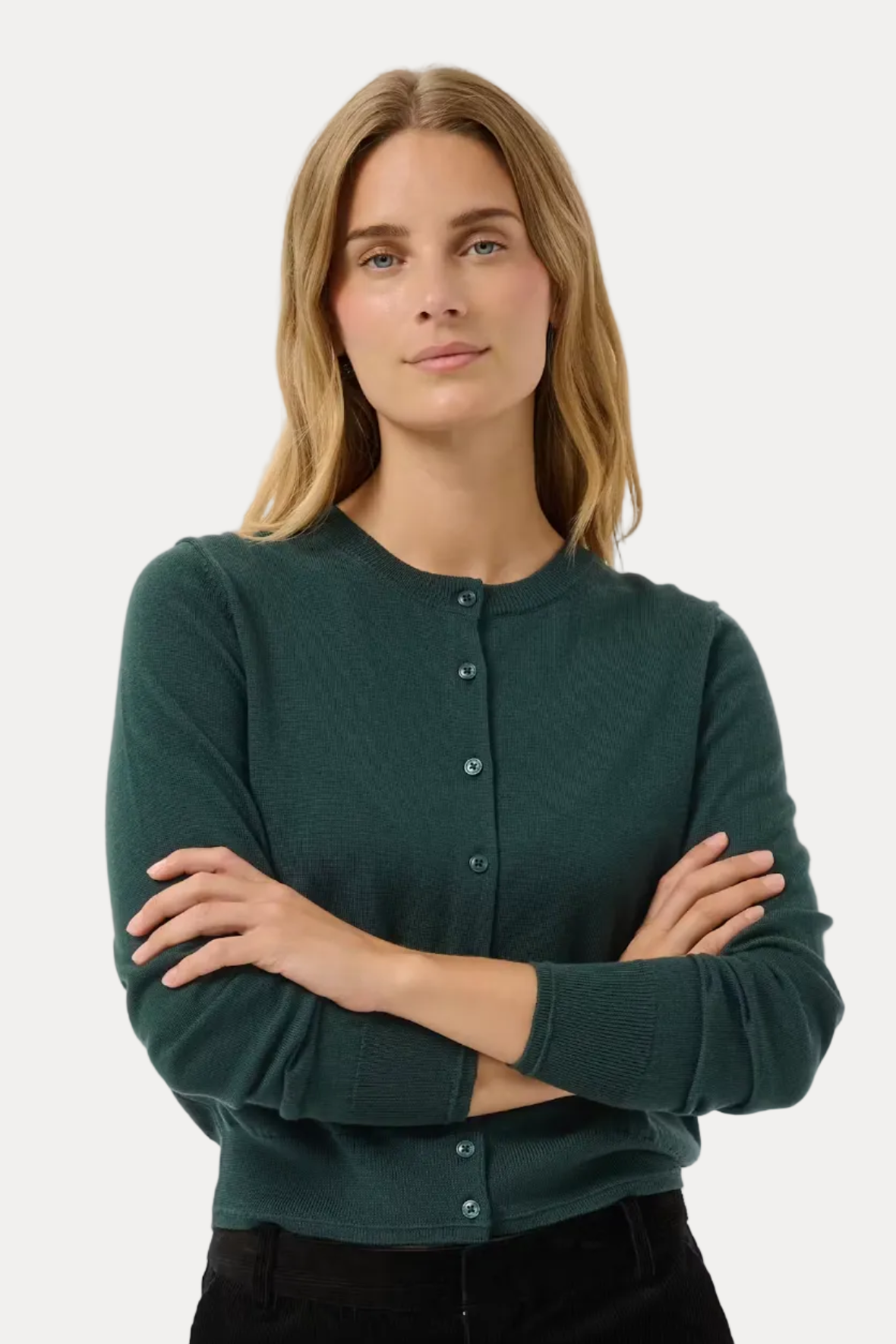 A woman modeling a dark green long-sleeve button-front cardigan with black pants, standing against a light gray studio background.