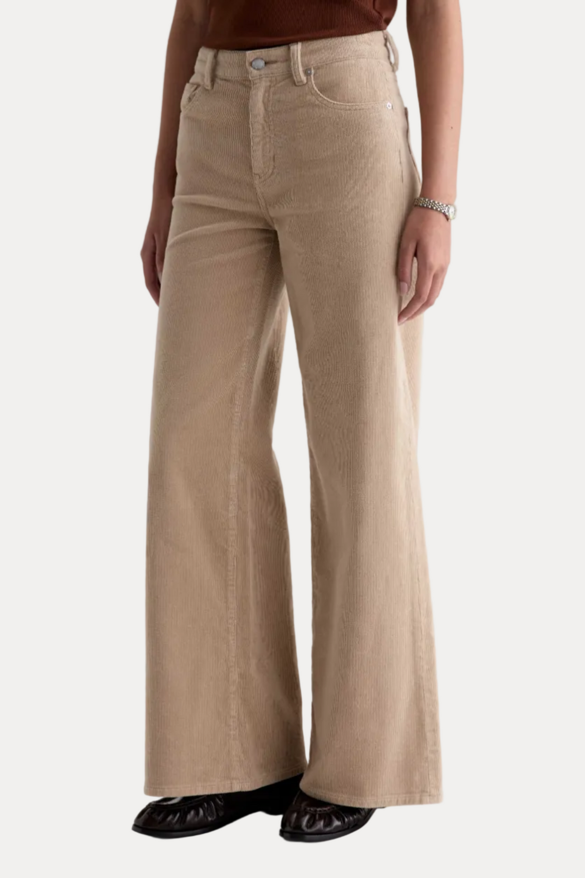 A model wearing a pair of beige wide-leg corduroy pants, paired with a brown top and black shoes, photographed against a clean white studio background.