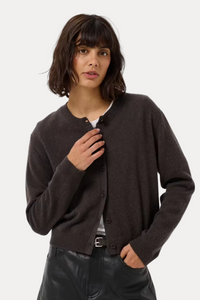 A woman modeling a dark brown button-up cardigan over a white top and a black faux-leather mini skirt, photographed against a light gray studio background.