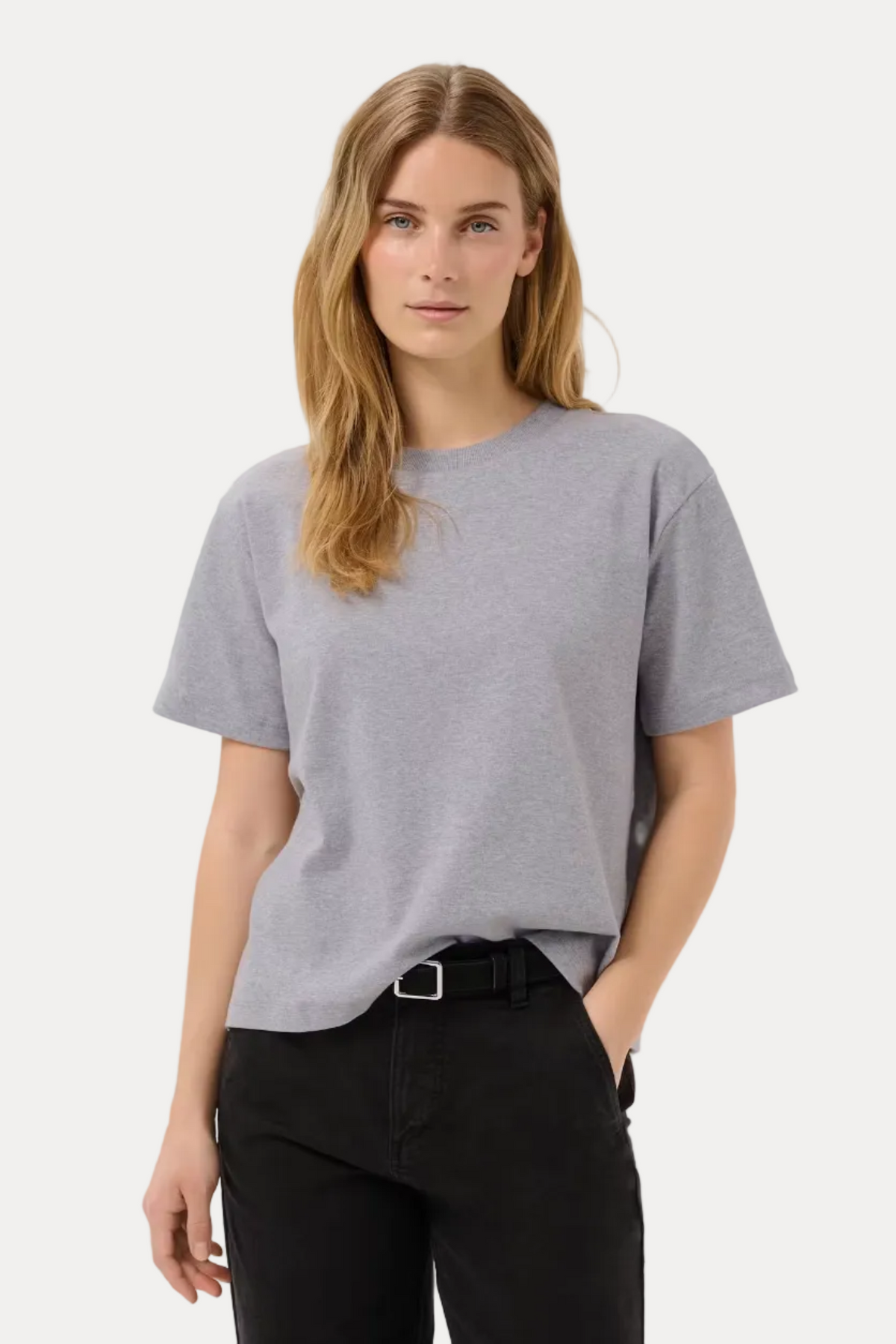 A woman modeling a light gray short-sleeve crewneck t-shirt paired with black pants and a black belt, photographed against a clean white studio background.