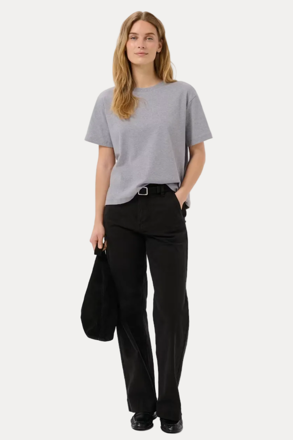 Person wearing a gray t-shirt and black pants holding a black bag on a white background