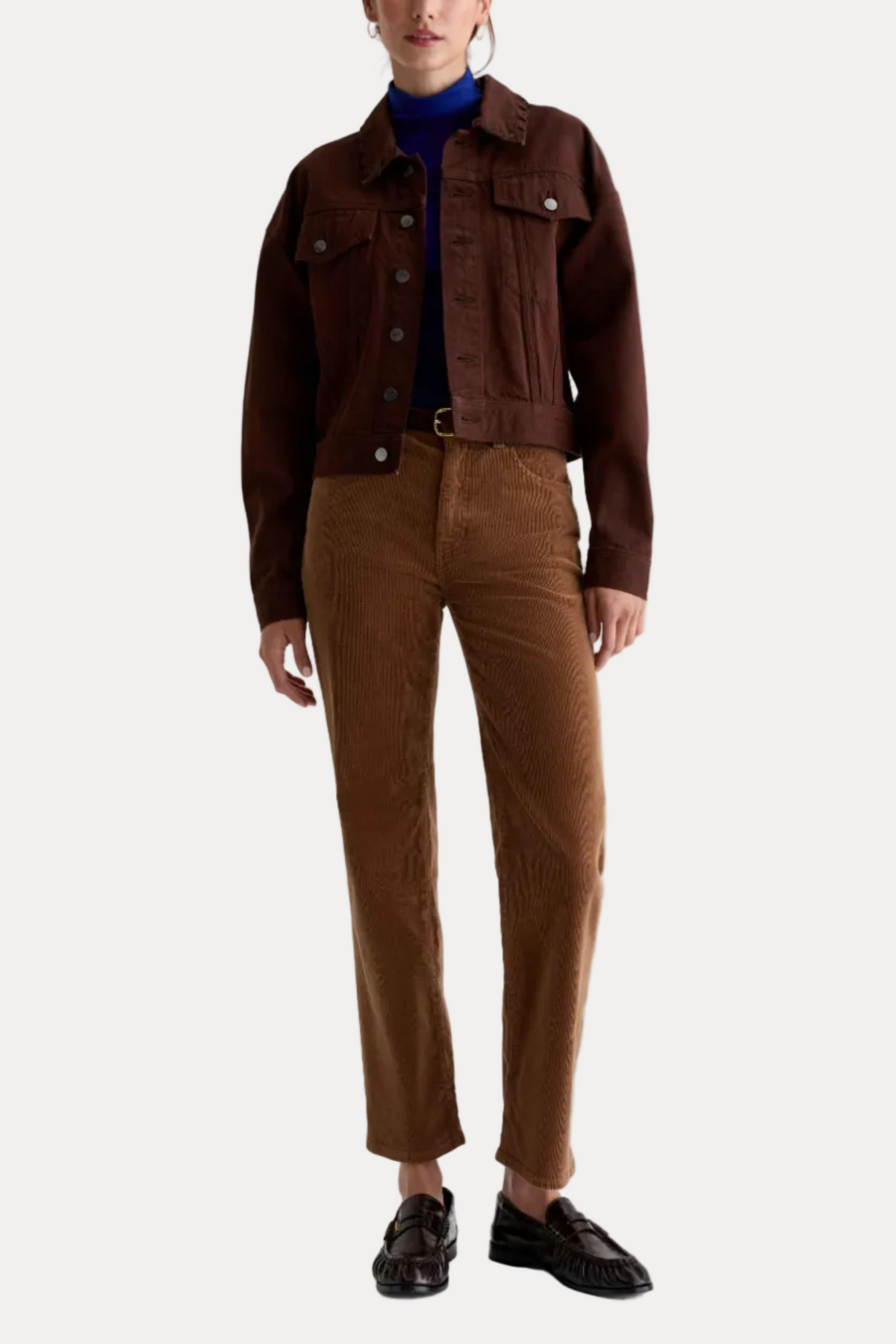 A model is shown from the neck down wearing a dark brown cropped denim jacket, a blue turtleneck, brown corduroy trousers, and dark brown loafers, shot against a plain white studio background.