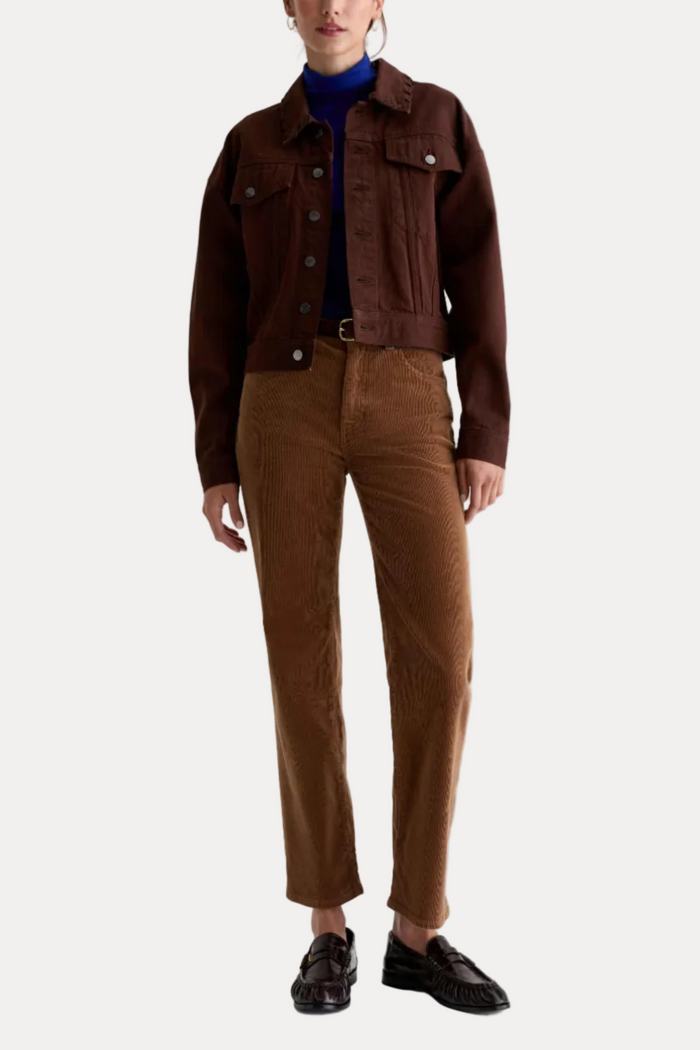 A model is shown from the neck down wearing a dark brown cropped denim jacket, a blue turtleneck, brown corduroy trousers, and dark brown loafers, shot against a plain white studio background.