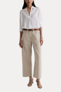 A model wearing a white long-sleeve button-down shirt, beige wide-leg cropped pants, a brown leather belt, and beige strappy high-heeled sandals, standing against a plain off-white studio background.