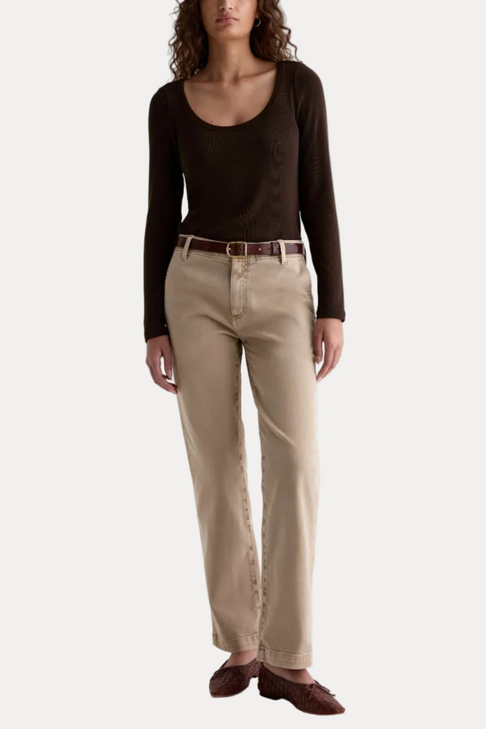 A model wearing a dark brown scoop-neck long-sleeve top, beige straight-leg jeans with a brown belt, and brown leather loafers, shot against a plain white studio background.