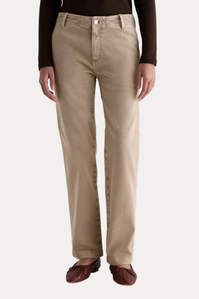 A person wearing straight-leg beige chinos with a dark brown long-sleeve top and dark brown leather loafers, shown from the waist down against a plain white studio background.