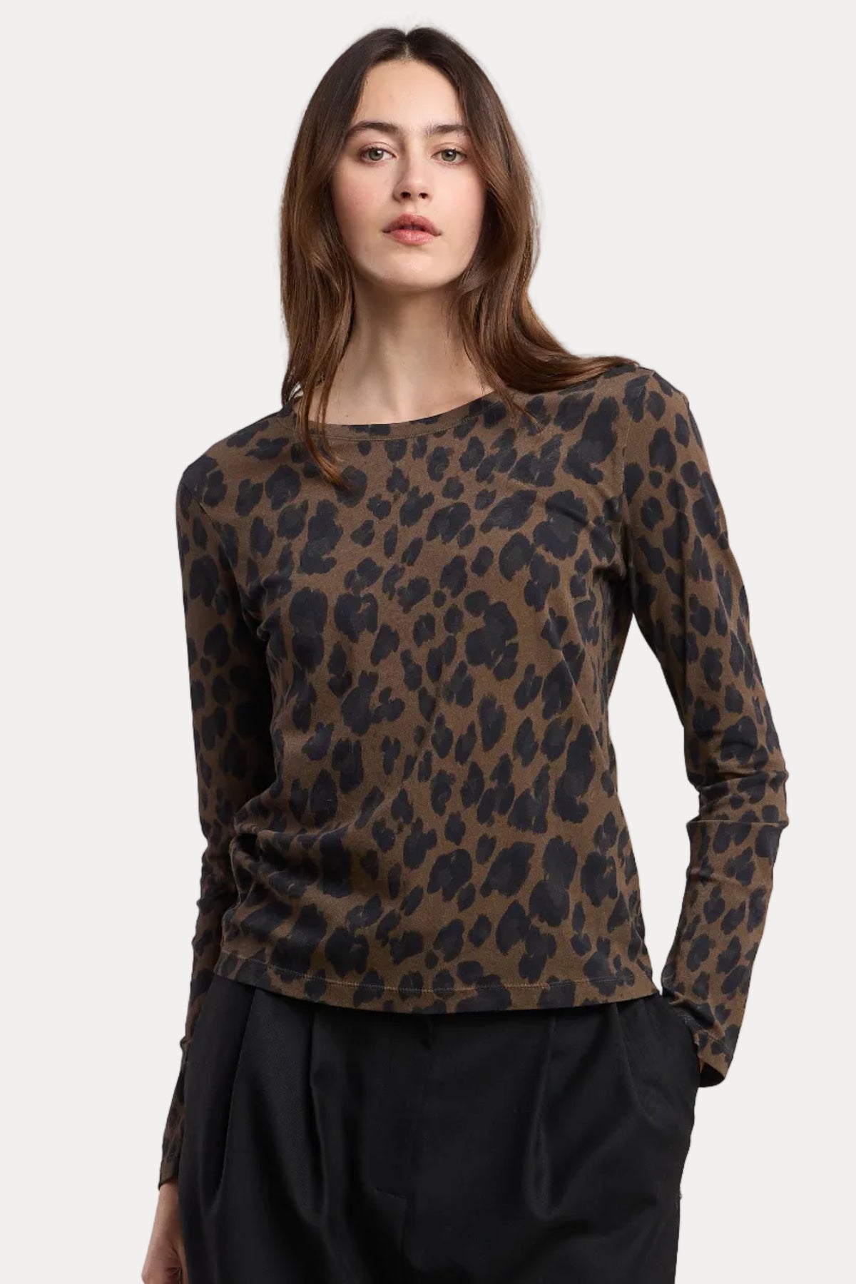 A woman modeling a brown and black leopard print long-sleeve top with black pants, photographed against a plain beige studio background.