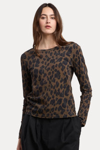 A woman modeling a brown and black leopard print long-sleeve top with black pants, photographed against a plain beige studio background.
