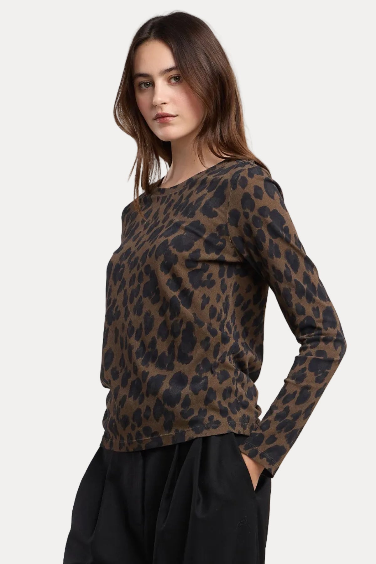 A woman modeling a brown and black leopard print long-sleeve top with black wide-leg pants, photographed against a solid light beige studio background.