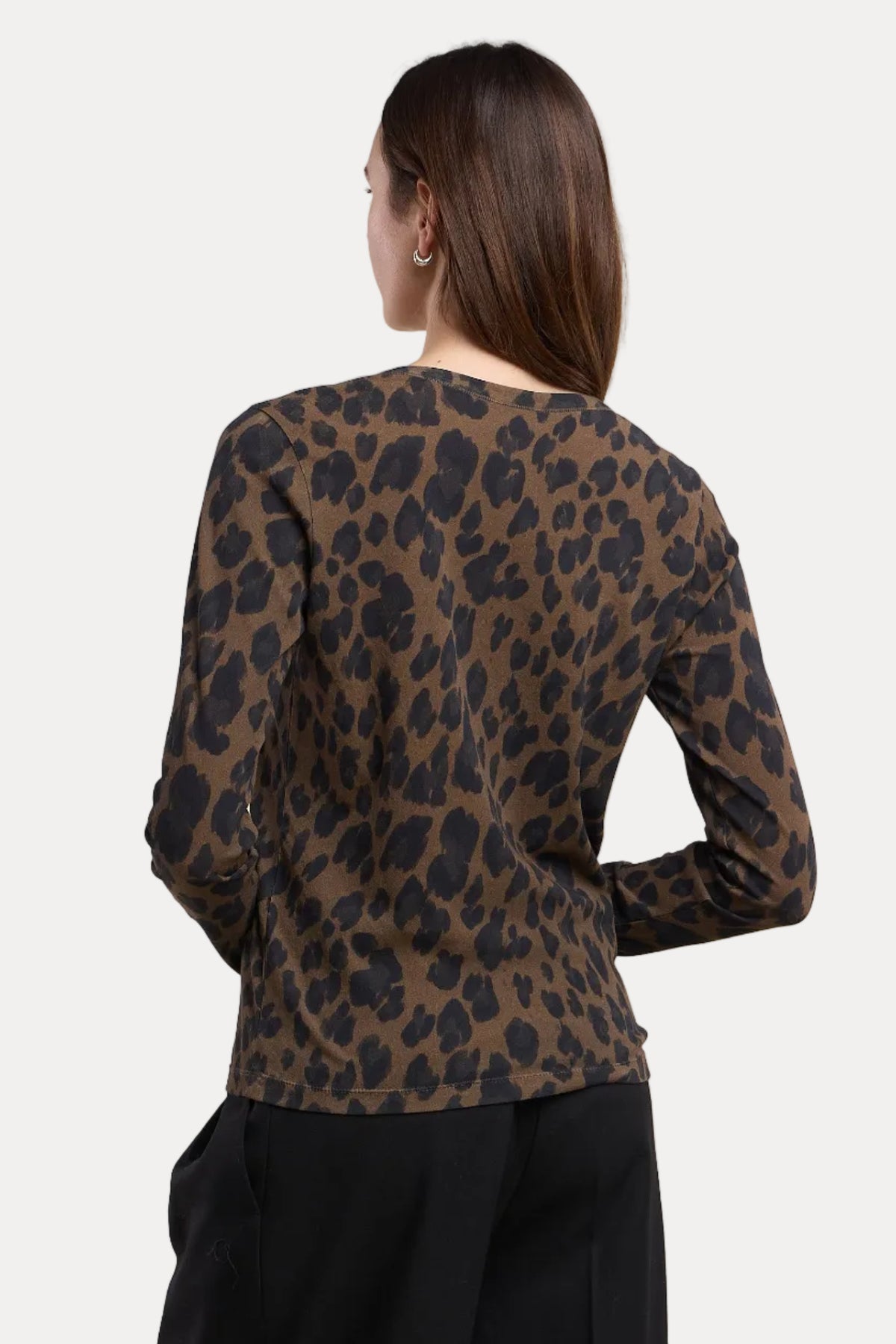 A woman shown from the back wearing a brown and black leopard print long-sleeve top with black pants, set against a plain beige studio background.