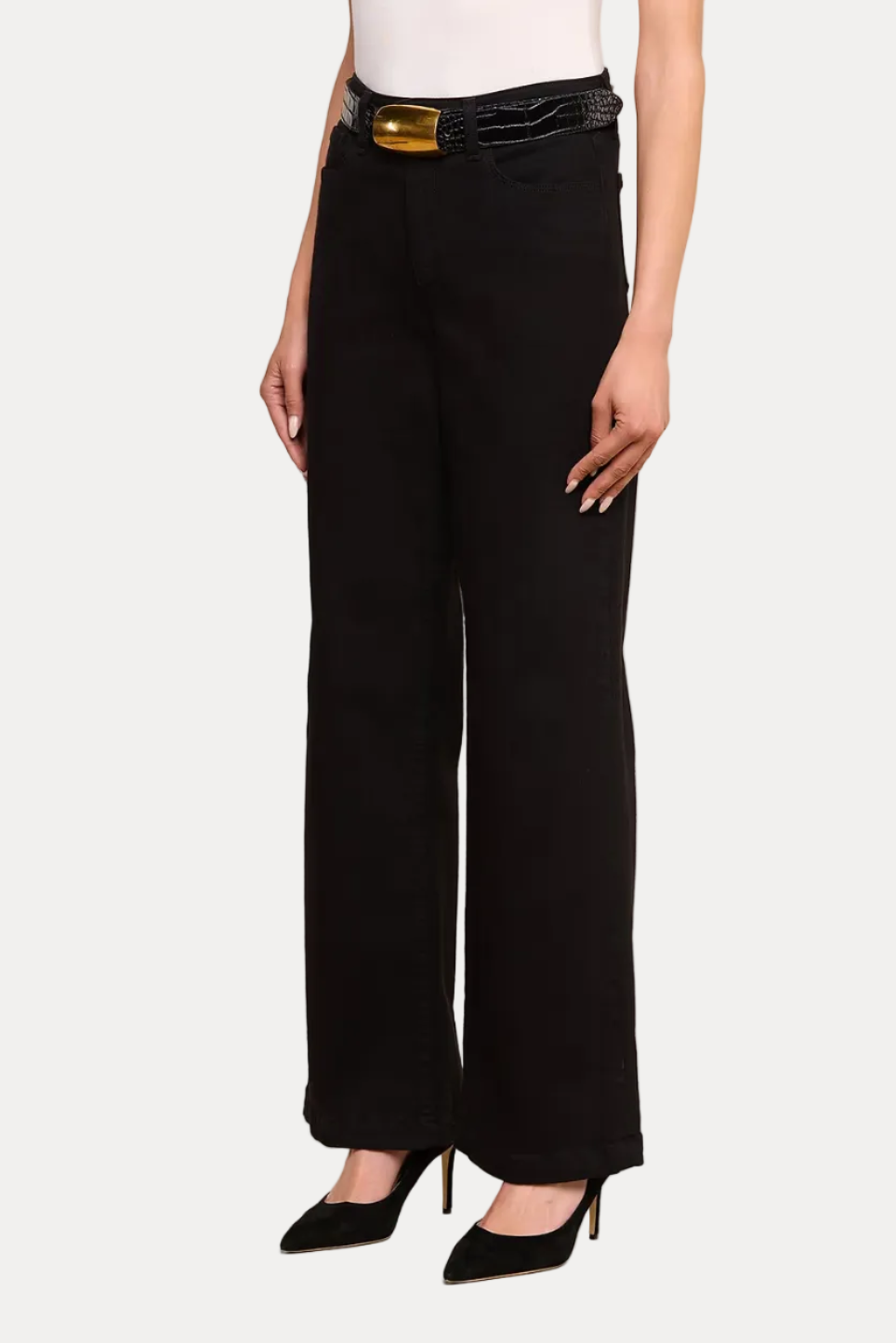 A model wearing black wide-leg trousers with a black belt featuring a gold buckle, styled with a white top and black pointed-toe heels against a plain white studio background.