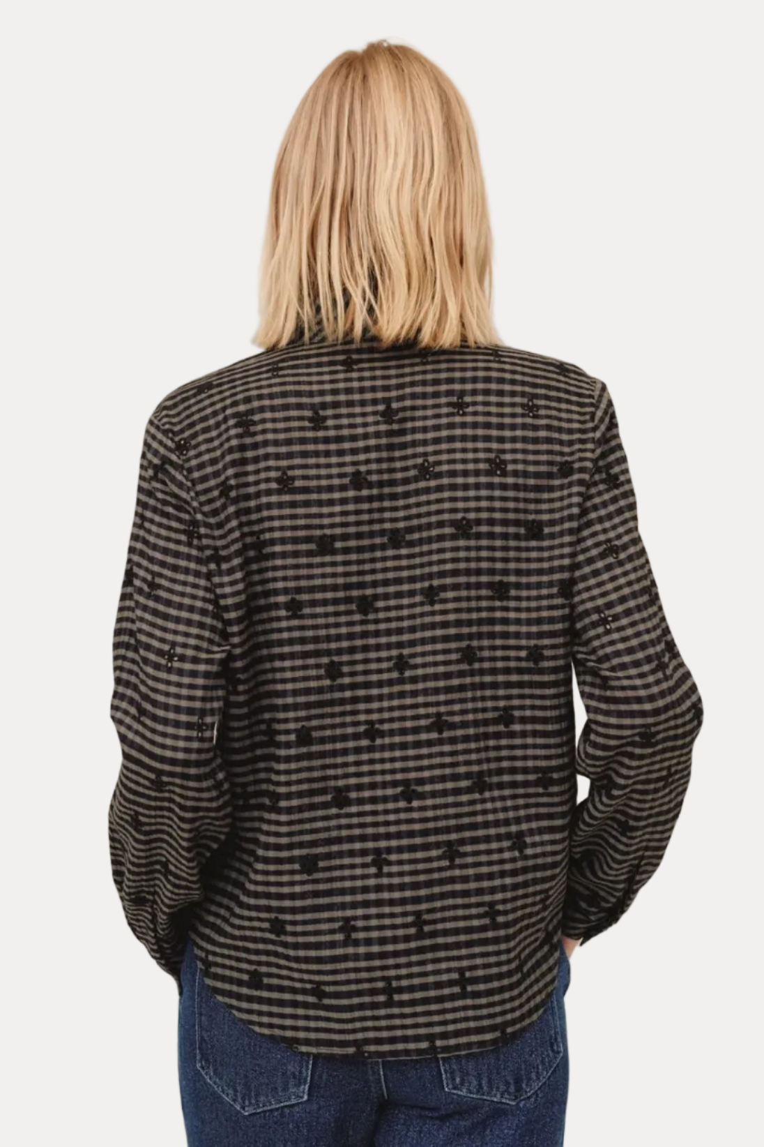 Person wearing a black and white checkered shirt with blue jeans on a beige background