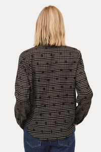 Person wearing a black and white checkered shirt with blue jeans on a beige background