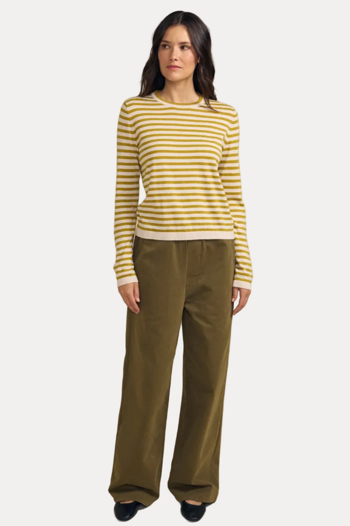 A woman modeling a yellow and white striped long-sleeve knit sweater with olive green wide-leg trousers, standing against a solid beige studio background.