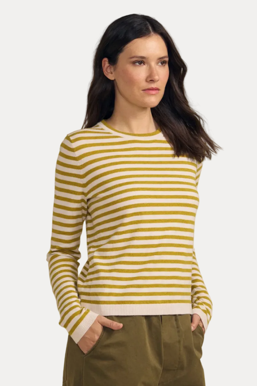 A woman modeling a yellow and white horizontally striped long-sleeve knit top with olive green pants, standing against a solid beige studio background.