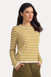 A woman modeling a yellow and white horizontally striped long-sleeve knit top with olive green pants, standing against a solid beige studio background.