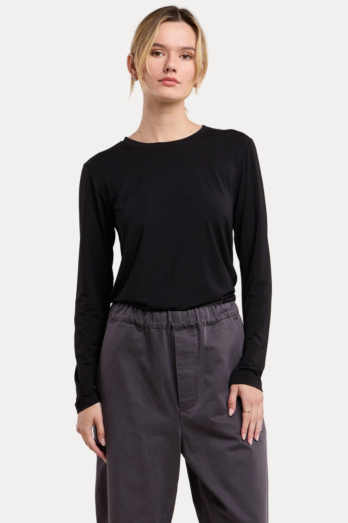 A woman modeling a black long-sleeve crewneck top paired with dark gray drawstring pants, set against a solid beige studio background.