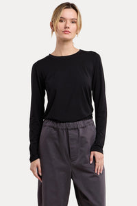 A woman modeling a black long-sleeve crewneck top paired with dark gray drawstring pants, set against a solid beige studio background.