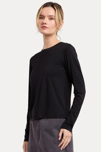 A woman modeling a black long-sleeve crewneck top paired with dark gray wide-leg pants, set against a plain beige studio background.