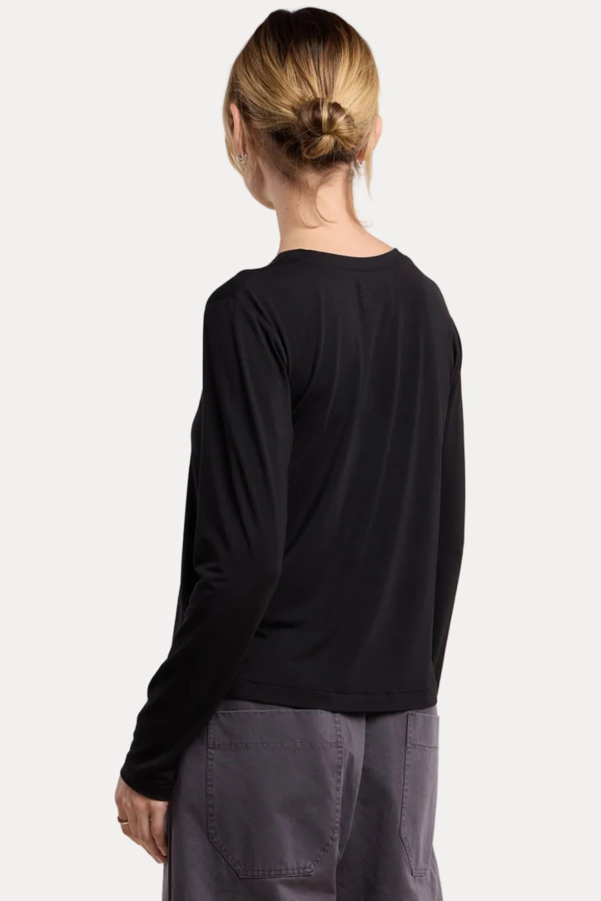 A woman shown from the back wearing a black long-sleeve crop top and dark gray wide-leg pants, photographed against a plain beige studio background.