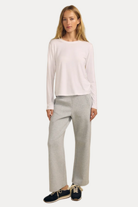 A woman modeling a white long-sleeve crewneck top and light gray wide-leg sweatpants, paired with navy blue sneakers, against a solid beige studio background.