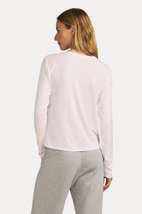 A woman shown from the back wearing a white long-sleeve top and light gray sweatpants, standing against a solid beige studio background.